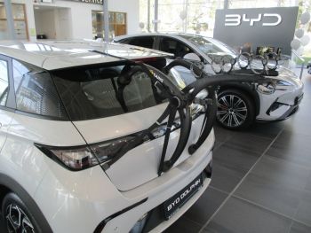 white byd dolphin in a byd showroom with a bike rack fitted to the tailgate photographed close at the rear from the side focusing on the bike rack 