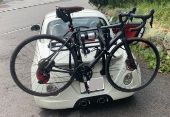 Rear view of a white Daihatsu copen with a bike rack fitted carrying a black racing bike