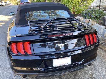 black ford mustang convertible parked next to a small stone wall on a sunny day photographed from the rear with a revo-rack black luggage rack fitted 