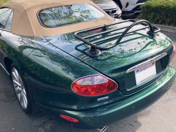 green jaguar xk8 convertible with a tan hood next to a hedge in a car park with a black luggage rack fitted to the trunk/boot lid