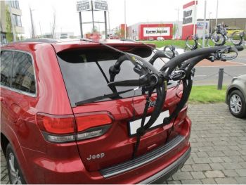 Burgundy Jeep Grand Cherokee with a bike rack fitted outside a car garage photographed close at the rear  focusing on the bike rack 