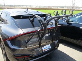 Grey Graphite Kia EV6 with a 3 bike rack fitted opposite a field photographed close at the rear to focus on the bike rack