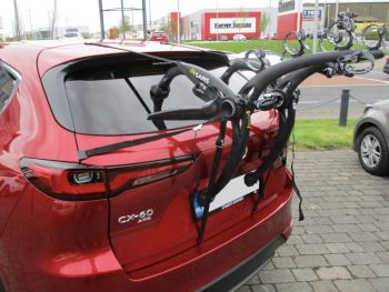 Burgundy Mazda CX-60 with a 3 bike rack fitted photographed close at the rear outside a Mazda garage 