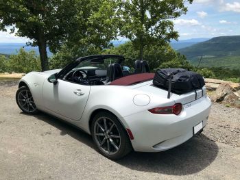 white mazda miata nd mx5 with the roof down next to a tree on a sunny day with a boot-bag luggage rack fitted to the trunk