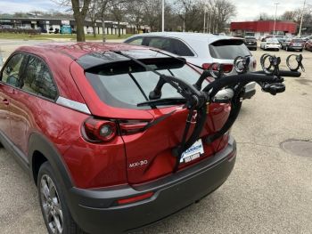 Burgundy Mazda MX-30 In car park opposite a store with a bike rack fitted photographed close at the rear focusing on the bike rack