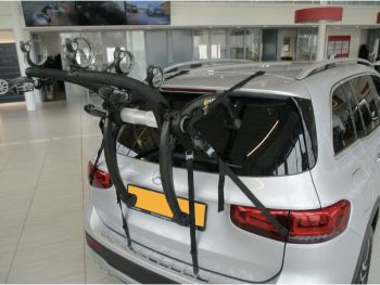 silver mercedes benz GLB with a 3 bike rack fitted to the rear in a car showroom photographed from the rear focusing on the bike rack