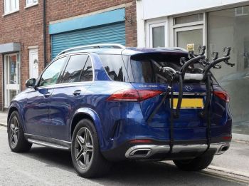 Blue Mercedes GLE with a 3 bike rack fitted parked opposite an empty shop photographed from the rear focusing on the bike rack