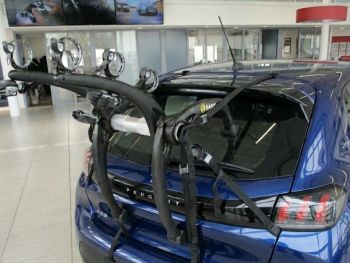 Bright blue peugeot 208 with a 3 bike rack fitted to the rear photogprahed in a car showroom close at the rear focusing on the bike rack