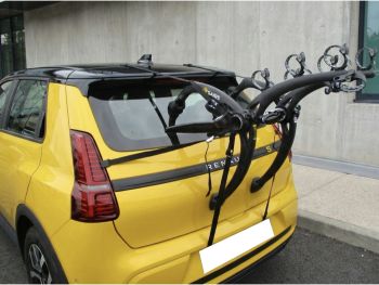 yellow renault 5 electric next to a concerete building with a bike rack fitted photographed from the rear to focus on the rack 