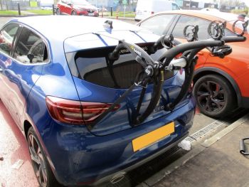 Blue Renault clio photogprahed from the rear with a 3 bike rack fitted outside a garage in a car park