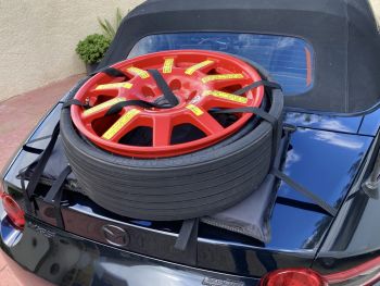 black mazda mx5 with a boot-bag spare wheel carrier fitted carrying a large red wheel photographed close at the rear 