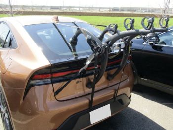 bronze 2024 Toyota Prius with a bike rack fitted photographed close from the rear in a car park opposite a grassy area