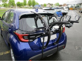 blue toyota yaris 2021 model year with a bike rack fitted parked outside a garage photographed from the rear to focus on the bike rack