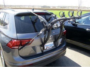 Graphite volkswagen VW Tiguan with a 3 bike rack fitted to the rear parked opposite a sports filed on a sunny day photogprahed from the rear focusing on the bike rack