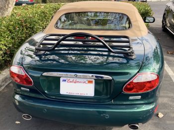 green jaguar xk8 convertible with a tan hood next to a hedge in a car park with a black luggage rack fitted to the trunk/boot lid