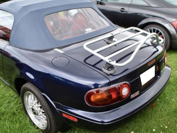 blue miata na with a red interior and a revo-rack stainless steel luggage rack fitted to the trunk parked on grass photographed close from the rear 