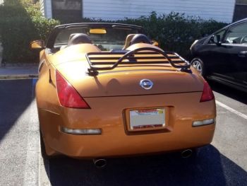 bronze nissan 350z roadster with a luggage rack fitted to the trunk outside a condo building in the sunshine