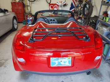 Red pontiac solstice in a garage with a revo-rack black luggage rack fitted photographed close from the rear next to a silver sedan